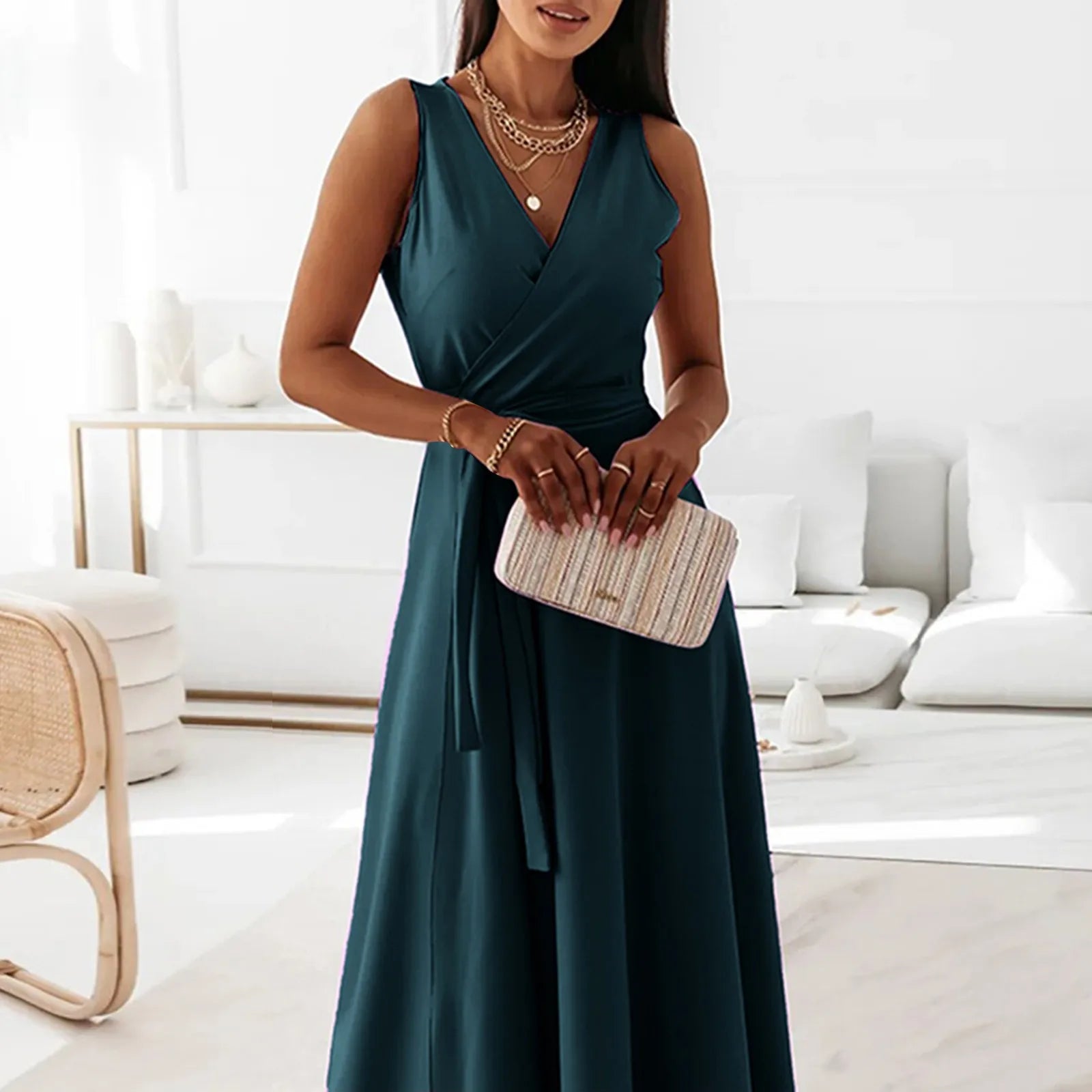 Woman in a teal dress holding a clutch in a modern living room.