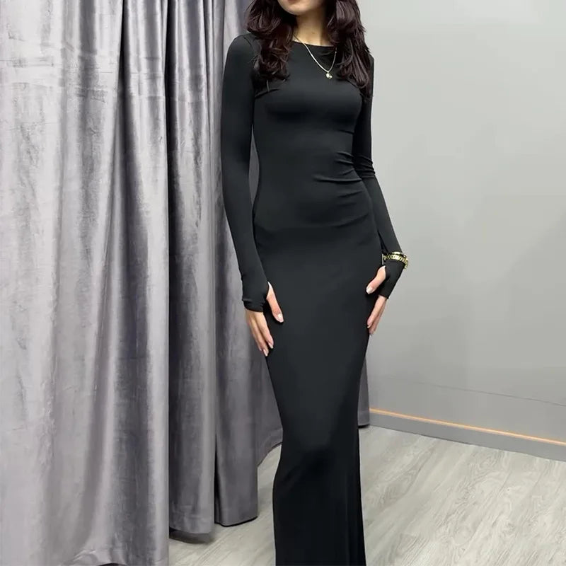 Woman wearing a black dress with long sleeves in front of gray curtains.