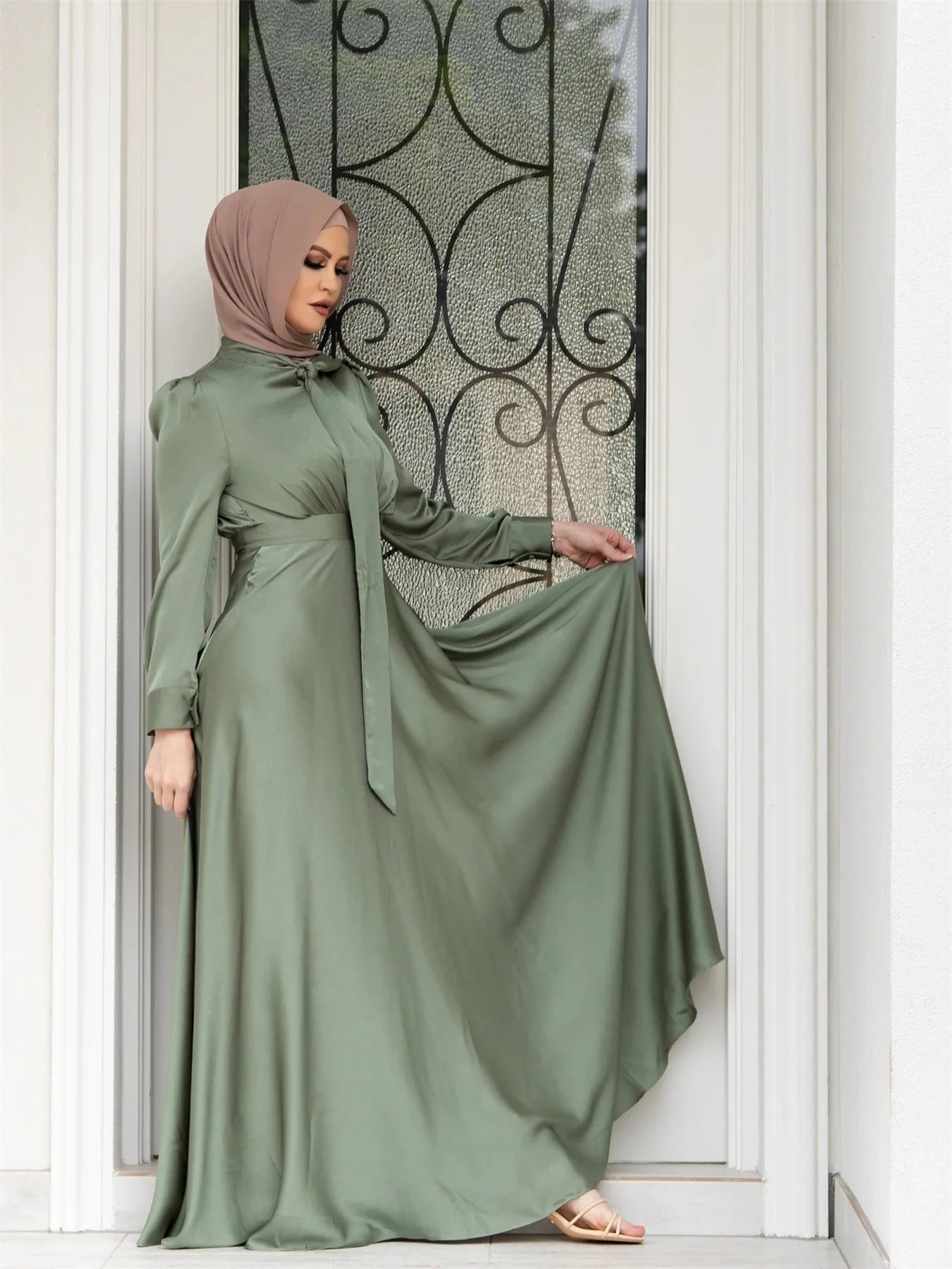Woman wearing a green dress with a matching hijab standing in front of a decorative glass door.