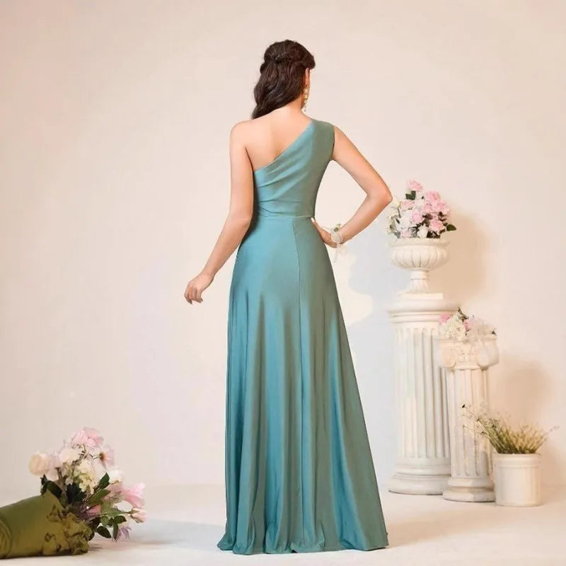 Woman wearing a teal one-shoulder dress in an elegant indoor setting with floral decorations.