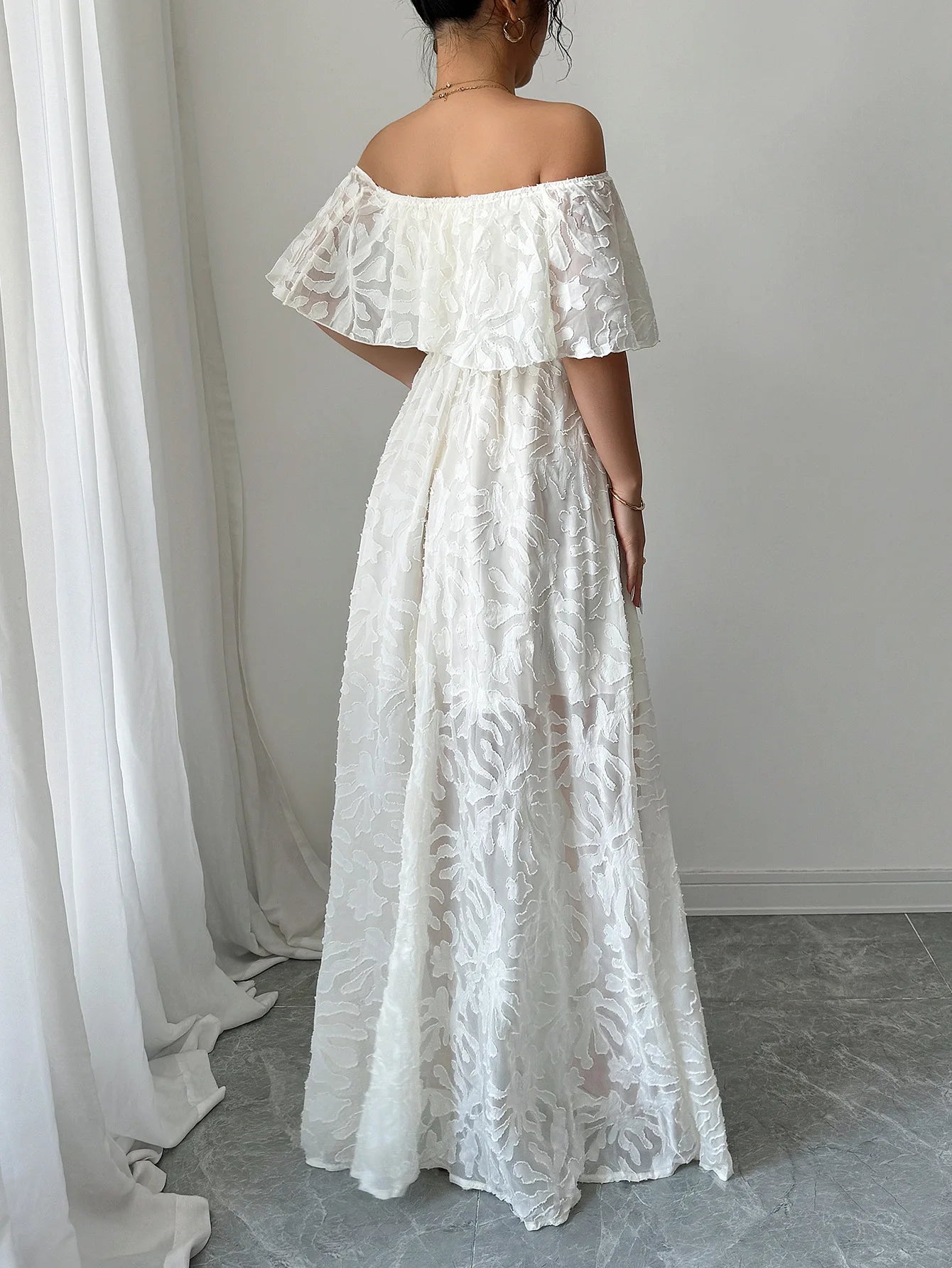 Woman wearing a white lace off-shoulder dress in a minimal indoor setting.